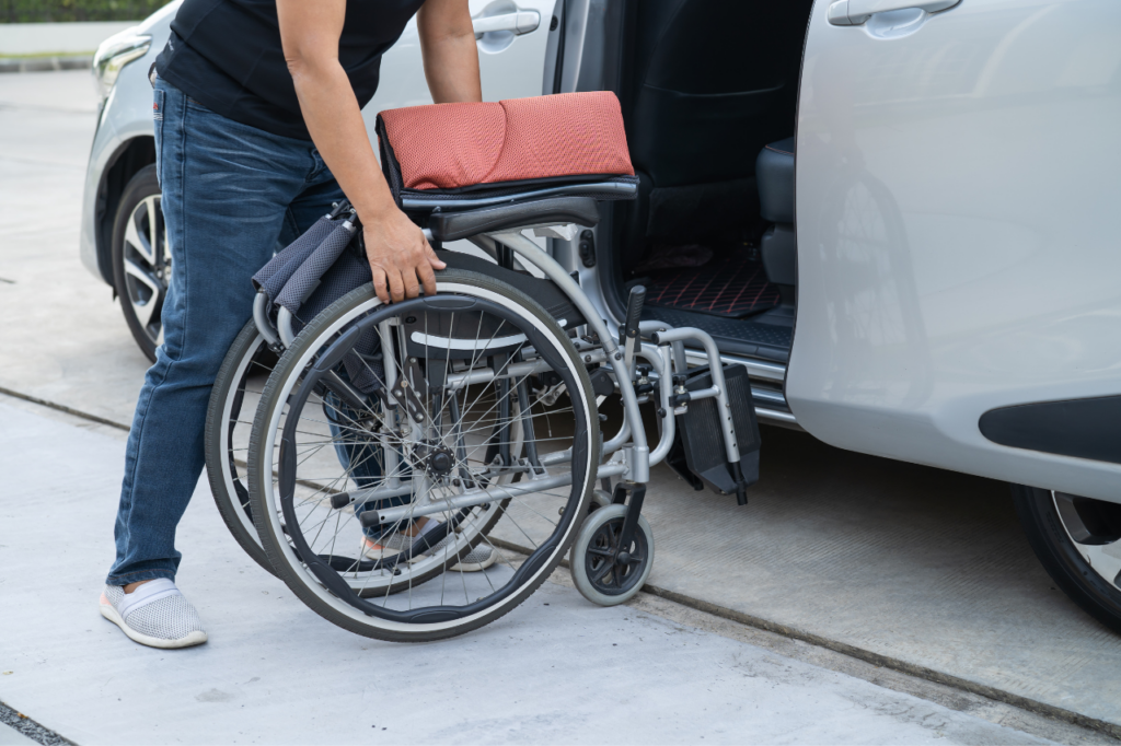 Un'assistente che carica una sedia a rotelle chiusa sul trasporto di ambulanza privata