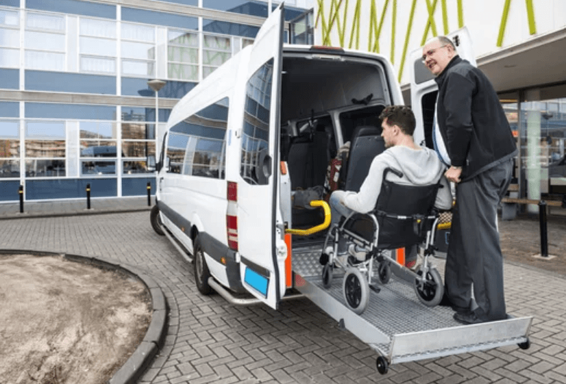 Un'assistente che aiuta un paziente su sedia a rotelle a salire sul taxi sanitario grazie all'ausilio della pedana